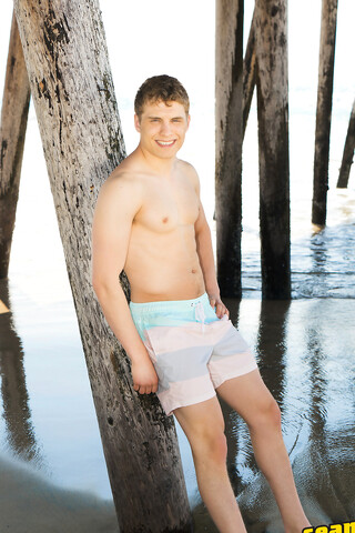Sexy Keiran poses on a beach before going inside and revealing his big cock